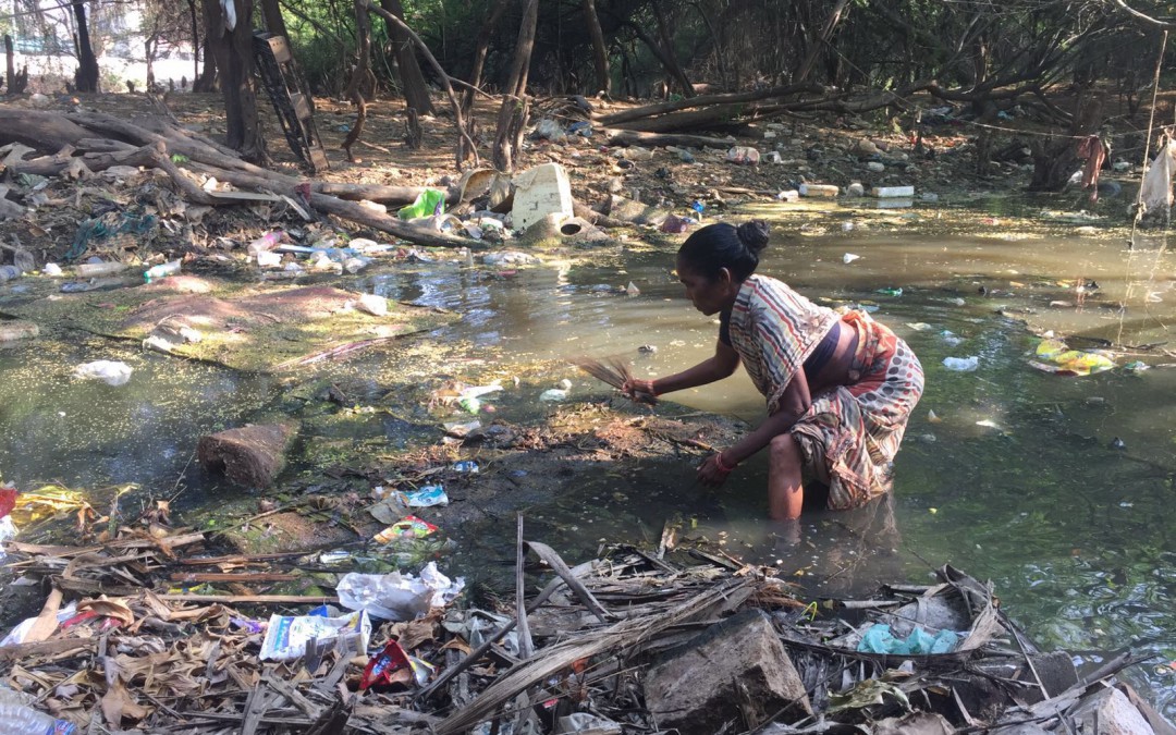 A survivor of the 2015 South India Floods clears debris from an inundated area around her home in the slums of Chennai, India.